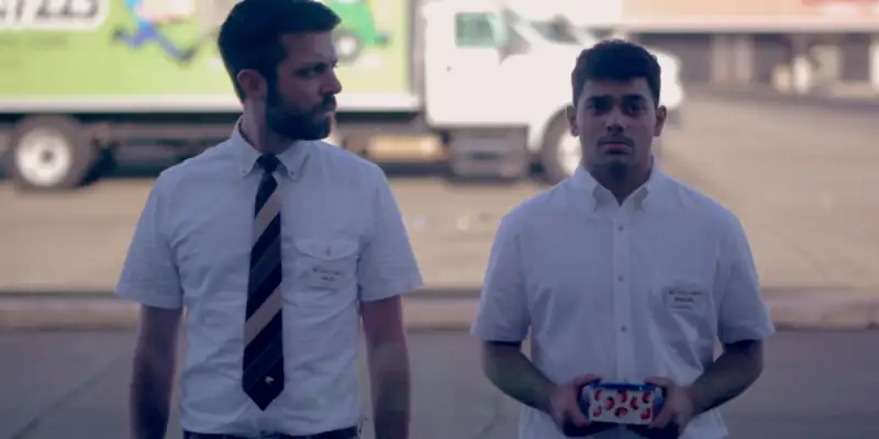 A scene from Nothing Really Happens where the main protagonist is standing on a sunny road with a colleague