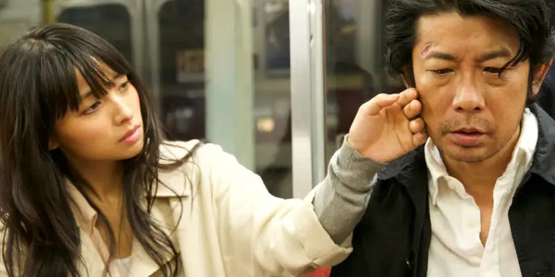 Misako caressing Masaya's cheek with the back of her hand as they sit on the train