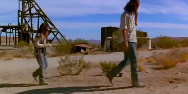 A scene from The Brave where Raphael is walking in contemplation in a dusty, hot desert, while his young daughter follows several steps behind