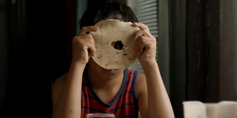 A scene from The Innocents 2021 showing Ben, a young boy, looking through a hole in a flat bread with one of his eyes